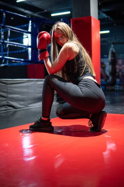 Blonde Caucasian fighter girl in Red Boxing Gloves is posing in Fight club training Hall