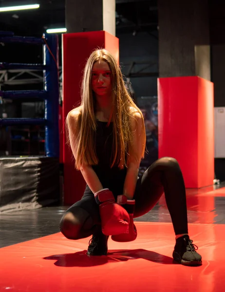 Blonde Caucasian fighter girl in Red Boxing Gloves is posing in Fight club training Hall