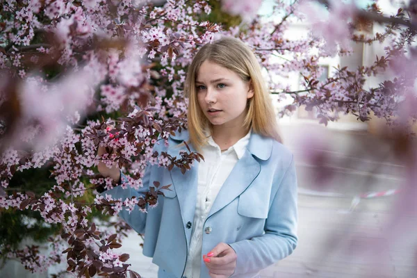 Porträt der schönen blonden Mädchen posiert in blühenden Zweigen mit rosa Blüten. Frühlingszeit — Stockfoto