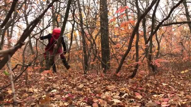 頭に大きな赤い頭蓋骨のマスクを持つ秋の森を通り抜ける古いスタイルの黒と赤のスケルトンの衣装を着た男. — ストック動画