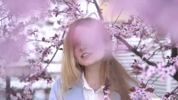 Retrato de Hermosa chica rubia posando en ramas de árboles florecientes con flores rosadas. Temporada de primavera — Vídeo de stock