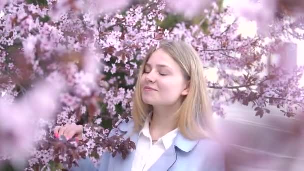 Porträtt av vacker blond flicka poserar i blommande trädgrenar med rosa blommor. Vårsäsongen — Stockvideo