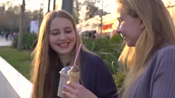 Zwei Freundinnen amüsieren sich am Abend auf der Breiten Straße. Eis essen und Eis mit frischem Milchshake trinken — Stockvideo
