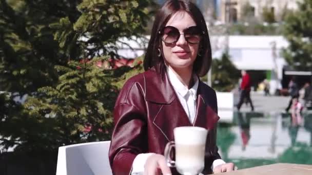 Het meisje in het café, in de buurt van een zwembad. een mooie jonge vrouw in Café drinken koffie latte onder zon licht op zonnige dag. — Stockvideo