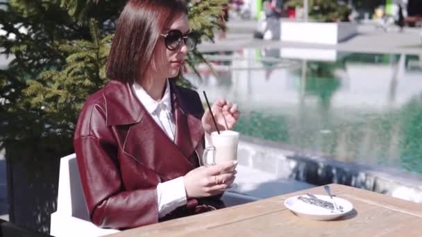 Het meisje in het café, in de buurt van een zwembad. een mooie jonge vrouw in Café drinken koffie latte onder zon licht op zonnige dag. — Stockvideo