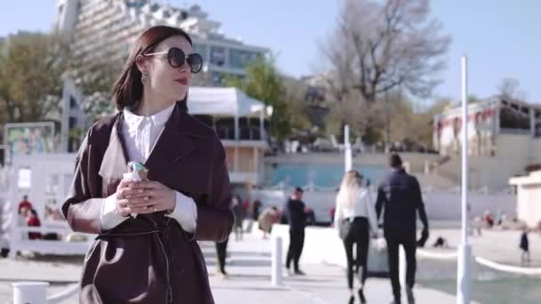 Roztomilá stylová brunetka, která chodí po nábřeží poblíž moře a konzumní zmrzlinu za slunečného dne — Stock video
