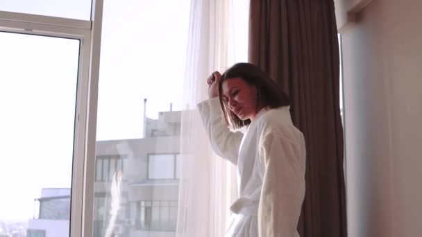 Mulher morena atraente em roupão de banho branco desfrutando de seus novos apartamentos para férias no piso 21 — Vídeo de Stock