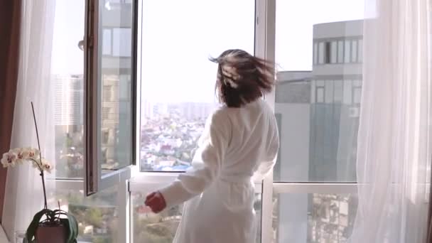 Attractive brunette woman in white bathrobe enjoying her new apartments for vacation. Happy Girl Dancing and falling on sofa. — Stock Video