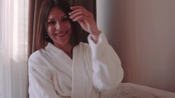 Portrait of young brunette woman in white bathrobe enjoying her new apartments. Posing and dancing on Sofa — Stock Video