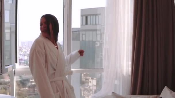 Atractiva mujer morena en albornoz blanco disfrutando de sus nuevos apartamentos para vacaciones en el piso 21 — Vídeos de Stock