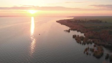Gün batımında yeşil tarlalarla çevrili büyük gölün üzerinde uçmak. Gölet ve liman sazlık ve kurbağalar ile