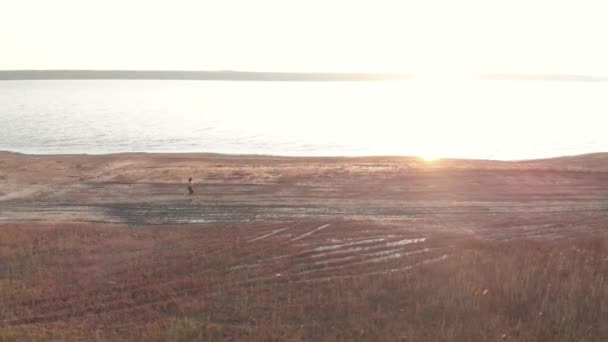 Tiro aéreo de jovem mulher esportiva correndo ao ar livre perto do lago ou liman durante o belo nascer do sol ou pôr do sol — Vídeo de Stock