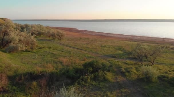 Tiro aéreo de jovem mulher esportiva correndo ao ar livre perto do lago ou liman durante o belo nascer do sol ou pôr do sol — Vídeo de Stock