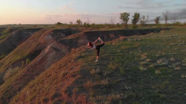 Повітряний постріл молодої спортивної жінки, що робить вправи на вершині схилу біля озера або лиману під час красивого сходу або заходу сонця — стокове відео
