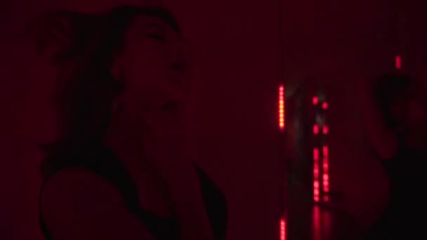 O tânără frumoasă femeie în rochie de coctail negru dansând lângă oglindă cu lămpi de neon. Club de moda mister tineresc beatiful fata zâmbitoare și seducătoare — Videoclip de stoc