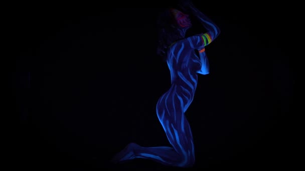Снимок обнаженной девушки в бодигарде, танцующей в ультрафиолетовом свете на черном фоне. Черный свет перчаток синий боди-арт авангард косплей дама с окрашенным ярким лицом — стоковое видео