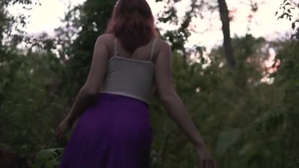 黄昏时分，年轻漂亮的女人穿着紫色的裙子赤着脚在树林里散步 — 图库视频影像