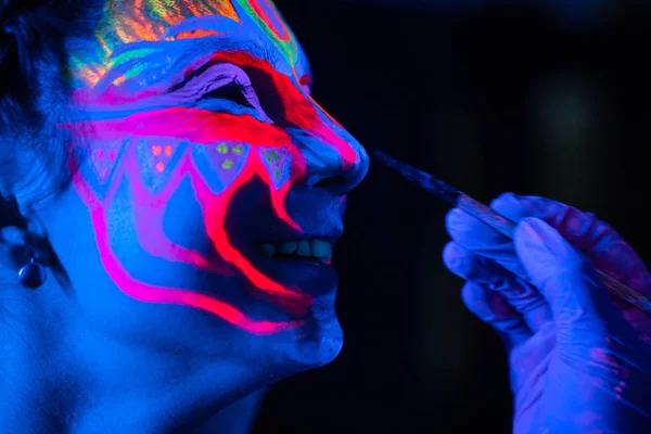 Ultraviolet black light glowing bodyart processing on young womans face. Pink and purple dyes in cold blue light — Stock Photo, Image