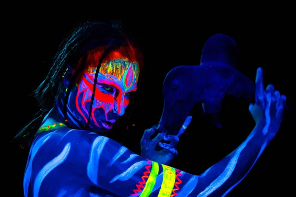 Portrait of Young naked bodyarted savage woman in blue glowing ultraviolet paint with primeval prehistorical tomahawk weapon. Agressive avatar warrior amazon with pigtails hairstyle