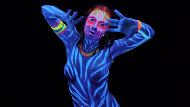 Молодая красивая обнаженная сексуальная девушка позирует в ультрафиолетовом свете на черном фоне. Черный свет перчаток окрашивает боди-арт авангардистки косплея с окрашенным ярким лицом — стоковое видео