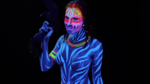 Portrait of Young naked bodyarted savage woman in blue glowing ultraviolet paint with primeval prehistorical tomahawk weapon. Agressive avatar warrior amazon with pigtails hairstyle — Stock Video