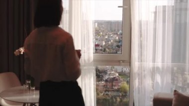 Çekici esmer kadın onu aromatik kahve zevk ve akşam evler yüksek kattaki pencerede bakıyor