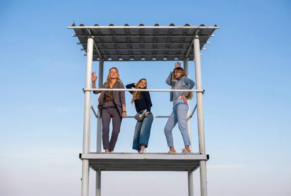 Trhree Jovens lindas meninas loiras em pantsuits elegantes estão dançando na torre de resgate na praia à noite — Fotografia de Stock