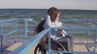Tekerlekli sandalyede engelli ler için rampada deniz kenarında dinlenen genç engelli kadın