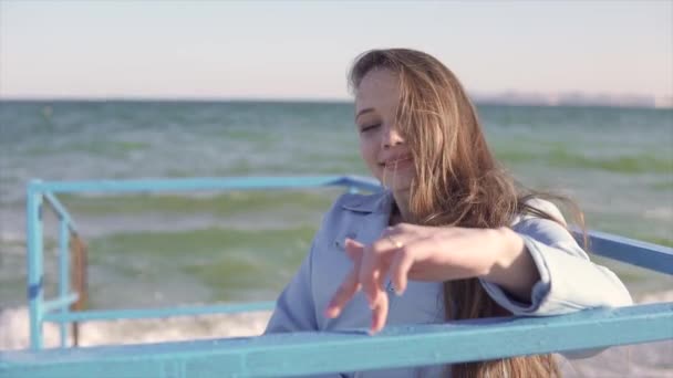 Joven mujer discapacitada en silla de ruedas muestra los dedos caminando por los pasamanos en la rampa para personas con discapacidad cerca del mar — Vídeos de Stock