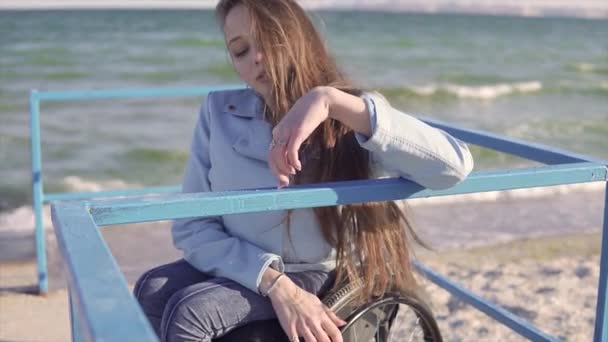 Młoda kobieta niepełnosprawna na wózku pokazuje palce krok pieszo przez poręcze na rampie dla osób niepełnosprawnych w pobliżu morza — Wideo stockowe