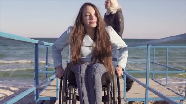 Giovane donna disabile in sedia a rotelle sta rotolando dalla rampa per le persone con disabilità vicino al mare — Video Stock