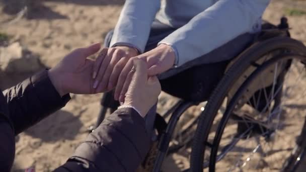 Familie vrije tijd. Jonge gehandicapte gehandicapte vrouw in rolstoel sprekende met haar moeder zittend in de buurt van de zee en houden elkaars handen — Stockvideo