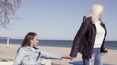Aile eğlencesi. Tekerlekli sandalyedeki genç engelli kadın, annesi yle birlikte deniz kenarında yürürken, konuşup eğleniyor