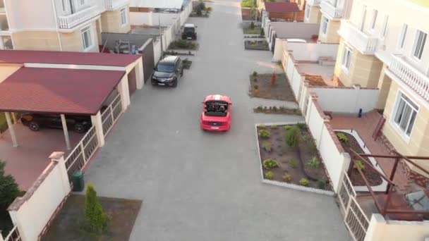 Ein erfolgreiches Paar im roten Cabrio-Sportwagen fährt am elitären Hüttendorf vorbei und parkt in der Nähe des Hauses mit roten Schindeln. Luftaufnahme. — Stockvideo