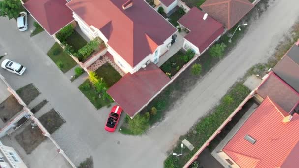 V Red kabriolet sportovní vůz se vyveze v elitní vesničce a Park nedaleko domova s červenými šindely. Letecká střela. — Stock video