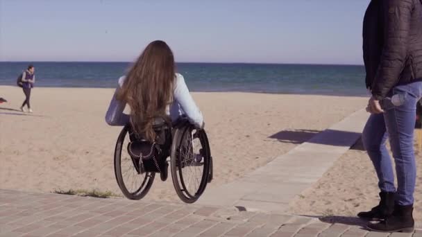 Young disabled woman in wheelchair moving by the wooden ramp for people with disabilities near the sea at spring or autumn time — Stock Video