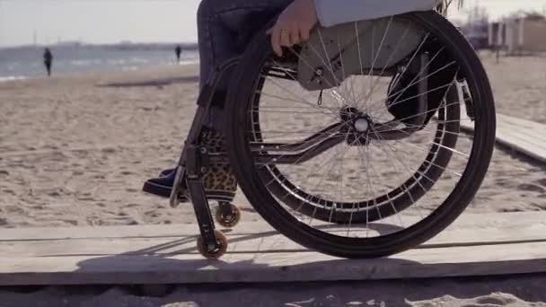 Joven mujer discapacitada en silla de ruedas que se mueve por la rampa de madera para personas con discapacidad cerca del mar en primavera u otoño — Vídeos de Stock