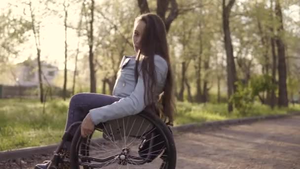 Jonge mooie gehandicapte vrouw in rolstoel wandelen in het Park 's avonds — Stockvideo