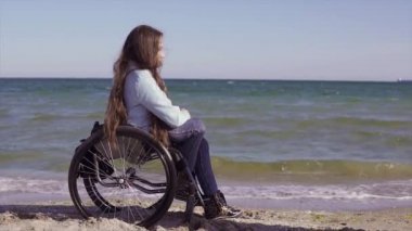 Anne ile tekerlekli sandalyede genç özürlü kadın deniz yakınındaki kum plajında eğlenmek