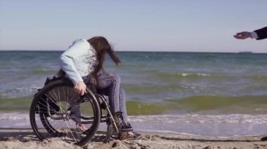 Anne ile tekerlekli sandalyede genç özürlü kadın deniz yakınındaki kum plajında eğlenmek