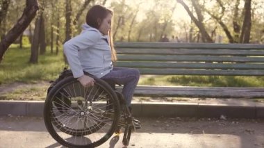 Tekerlekli sandalyede genç Pretty özürlü kadın koltukta parkta banch akşam zamanında hareket