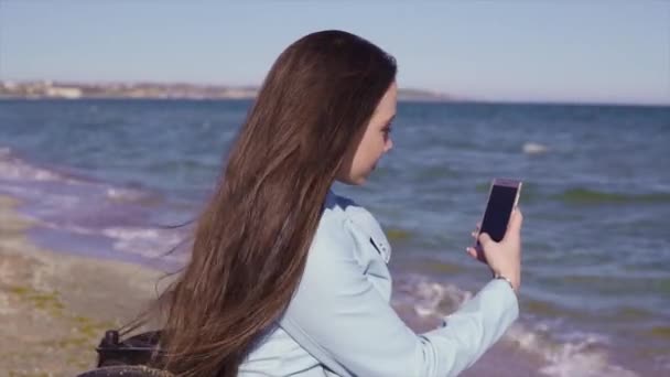Joven mujer con discapacidad en silla de ruedas divirtiéndose en la playa de arena cerca del mar. Disparando con su teléfono y haciendo selfie — Vídeos de Stock