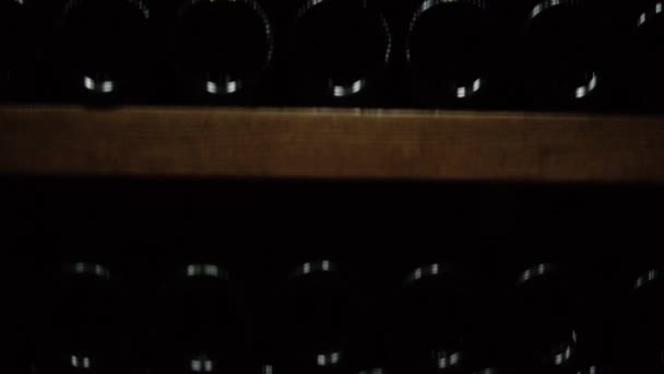 Vinflaskor ligger i stapeln i källaren. Glasflaskor rött vin lagrat i trä hyllor i stenkällare. Interiör underjordisk vinkällare i vingård — Stockvideo