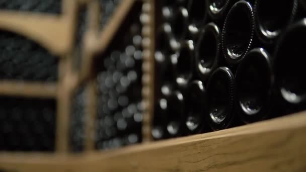 Винные бутылки лежат в стопке в подвале. Стеклянные бутылки красного вина хранятся на деревянных полках в каменном подвале. Подземный винный погреб в винном погребе — стоковое видео
