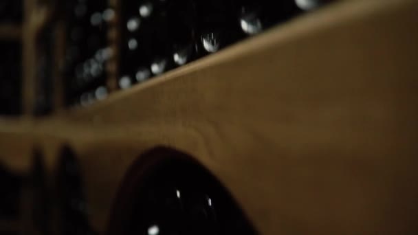 Bouteilles de vin couchées en pile à la cave. Bouteilles en verre de vin rouge stockées dans des étagères en bois dans une cave en pierre. Cave à vin souterraine intérieure dans la cave — Video