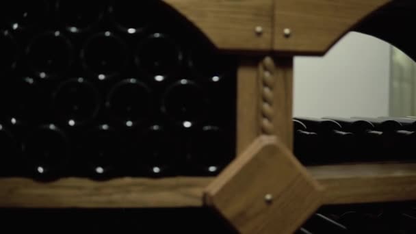 Wijnflessen liggen in stapel in de kelder. Glazen flessen rode wijn opgeslagen in houten planken in stenen kelder. Binnenondergrondse wijnkelder in wijnmakerij — Stockvideo