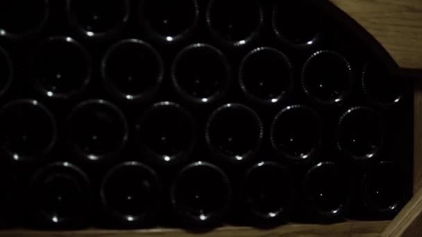 Primer plano de botellas de vino que yacen en la pila en la bodega. Botellas de vidrio de vino tinto almacenadas en estanterías de madera en bodega de piedra. Bodega interior subterránea en bodega — Vídeo de stock