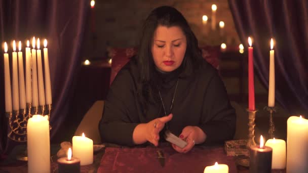 Женщина-предсказательница в темной комнате с кучей свечей угадывает на колоде карт Таро — стоковое видео