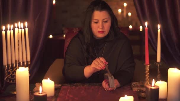 Женщина-предсказательница в темной комнате с кучей свечей угадывает на колоде карт Таро — стоковое видео