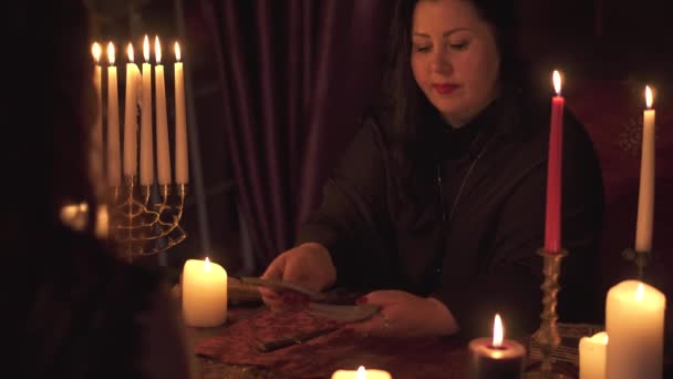タロットカードデッキにキャンドルの多くを推測する暗い部屋で占い師の女性 — ストック動画